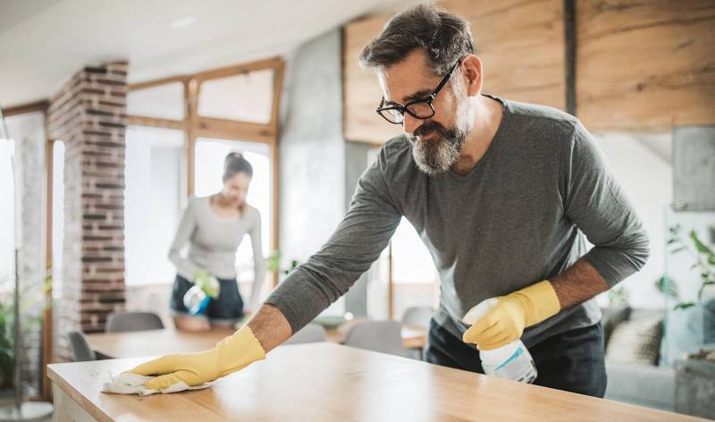 Men in brown t-shirt and yellow gloves scrubbing a table with spray and cloths