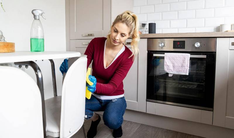 Woman in marron t-shirt and blue jeans scrubbing a white chair inside a room