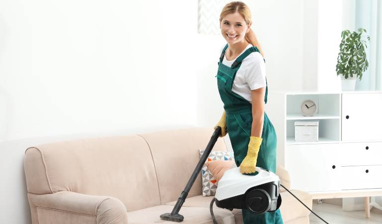 woman removing dust from sofa holding vacuum cleaner in her hand