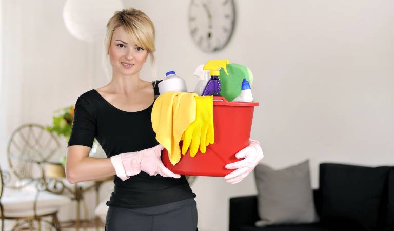 Woman in black dress holding a red basket filled with tools and supplies.