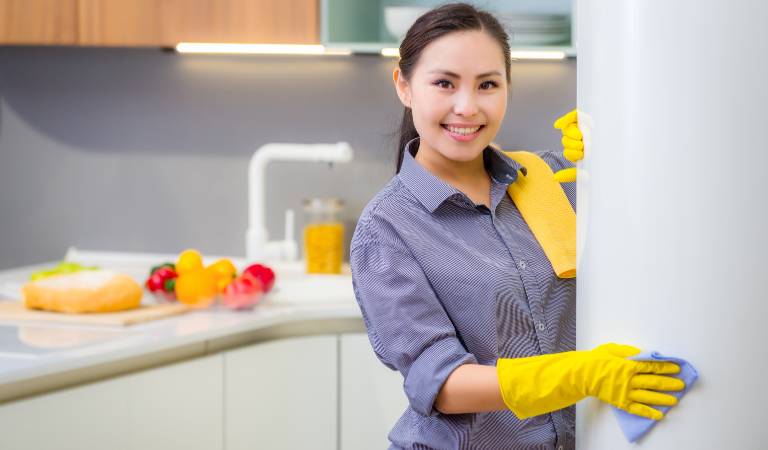 Woman in yellow gloves smiling inside a kitchen