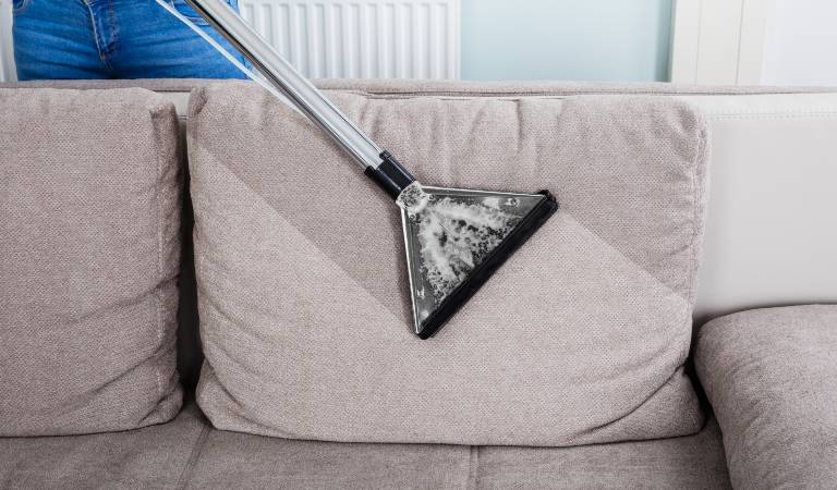 Woman using vacuum cleaner cleaning her velvet sofa