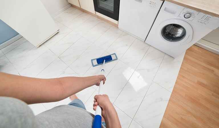 Woman is cleaning tiles inside kitchen with a cleaning stick