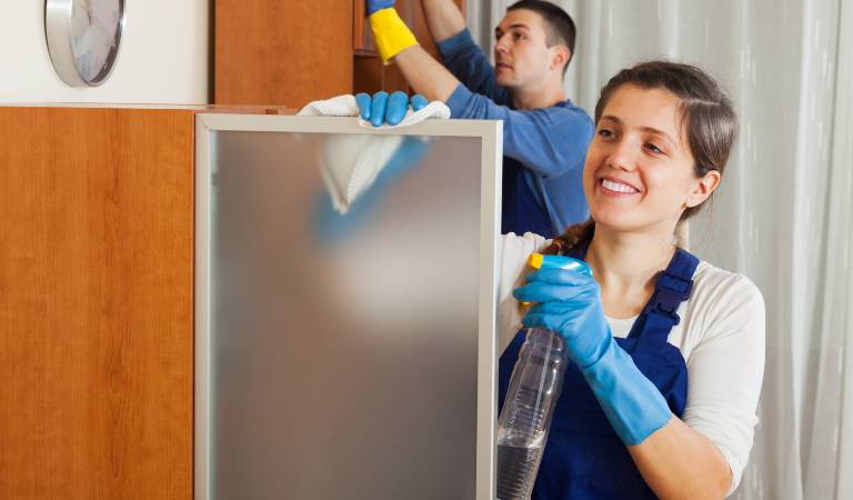 Woman and a man in black-white uniform performing bond cleaning task inside a room