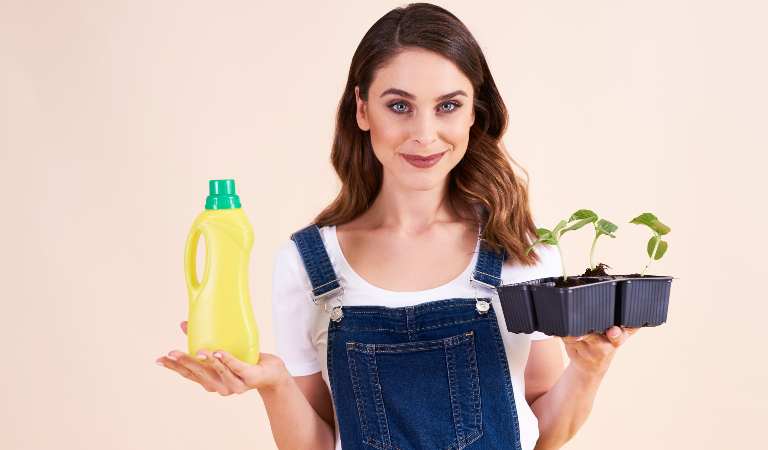 Woman holding a yellow bottle in one hand and plant in second hand.