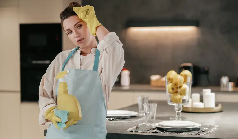 Woman in yellow gloves holding a spray bottle inside her kitchen.