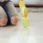 Woman in yellow gloves holding a bottle in her hand cleaning floor.