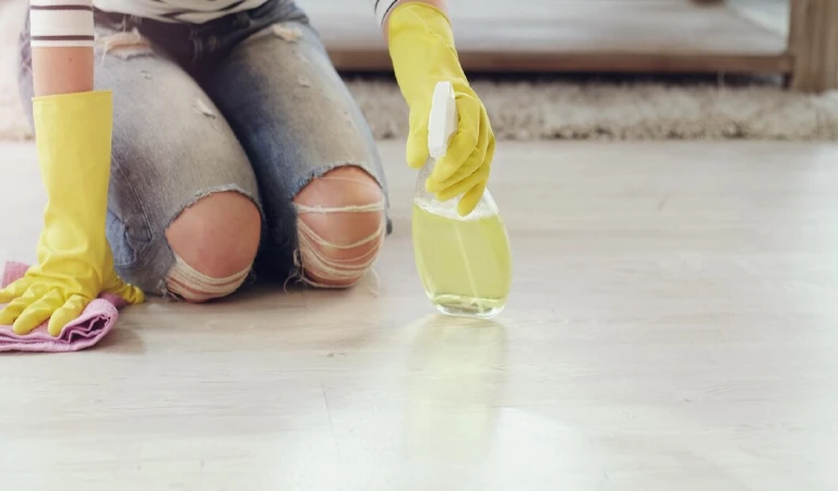 Woman in yellow gloves holding a bottle in her hand cleaning floor.