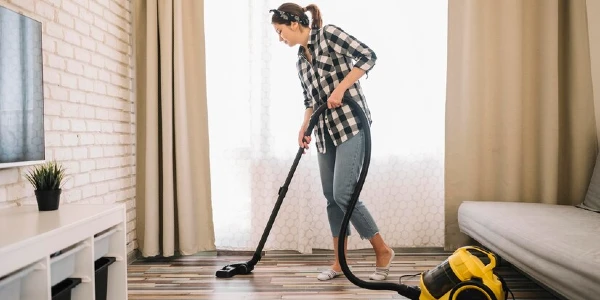 Lady in check shirt cleaning floor with a vacuum cleaner.