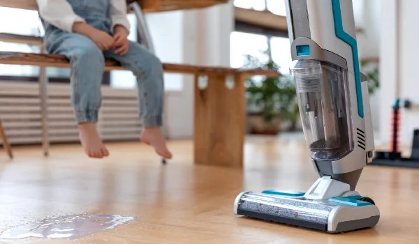 Cordless steam mop or vacuum cleaner cleans floor from yogurt and child on background