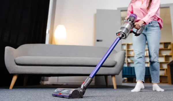 Young woman uses cordless vacuum cleaner to clean home carpet modern easy cleaning