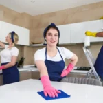 Professional cleaners in blue uniform washing floor and wiping dust from the furniture at apartment. Cleaning service concept