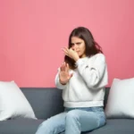 Bad smell young girl pinch nose showing stop gesture feel disgust sitting on sofa