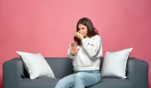 Bad smell young girl pinch nose showing stop gesture feel disgust sitting on sofa